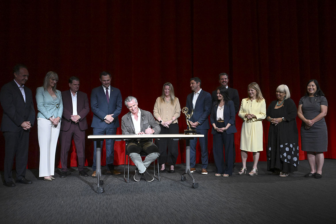 Members of the Advocacy Committee, Bobbi Banks and Christina Lee Storm, stand with California Post Alliance, union representatives, and key legislators as Governor Newsom signs AB2139.