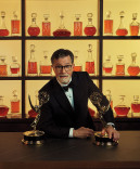 Stephen Colbery in a tuxedo poses with his two Emmy Awards