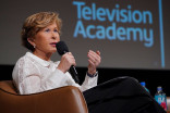 A woman holding a microphone in front of a large screen that reads "Television Academy"