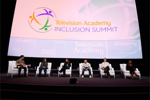 6 people sitting in white chairs in front of a large screen