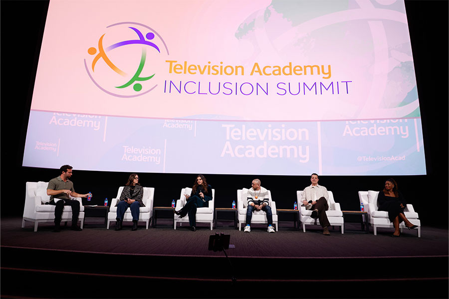6 people sitting in white chairs in front of a large screen