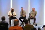 Three men sitting on stool holding microphones and speaking to an audience