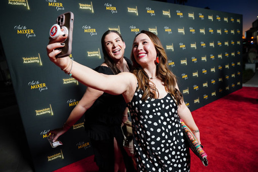Two women on a red carpet taking a selfie with a phone